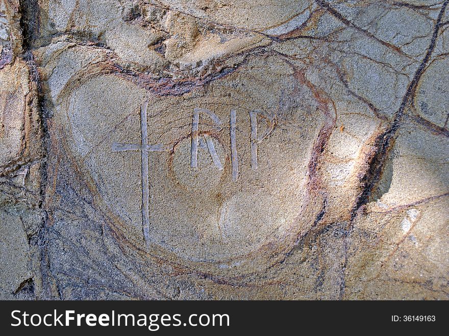 Cross and letters RIP carved into rock of cliff side. Cross and letters RIP carved into rock of cliff side