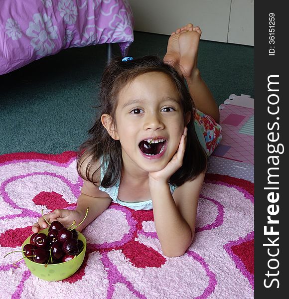 A young Asian girl relaxes on her bedroom floor and enjoys eating fresh cherries. A young Asian girl relaxes on her bedroom floor and enjoys eating fresh cherries.