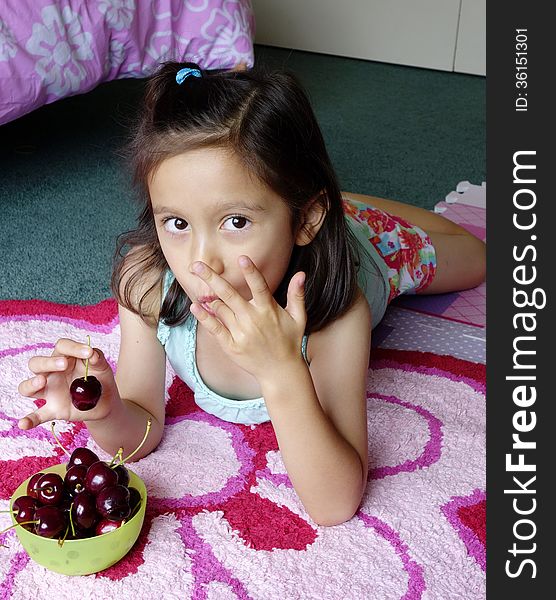 A young Asian girl lies on her bedroom floor as she licks the cherry juice from her fingers. She holds another cherry ready to eat. A young Asian girl lies on her bedroom floor as she licks the cherry juice from her fingers. She holds another cherry ready to eat.