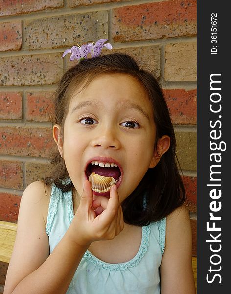 A young Asian girl delights in the thought of eating the chocolate she holds in her fingers. A young Asian girl delights in the thought of eating the chocolate she holds in her fingers.