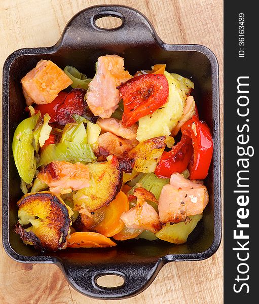 Tasty Homemade Salmon Stew with Potato, Red Bell Pepper, Leek and Carrot in Black Frying Pan on Wooden background. Top View