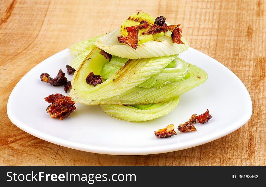 Stack Tasty Roasted Leek with Fried Tomatoes and Paprika on White Plate closeup on Wooden background