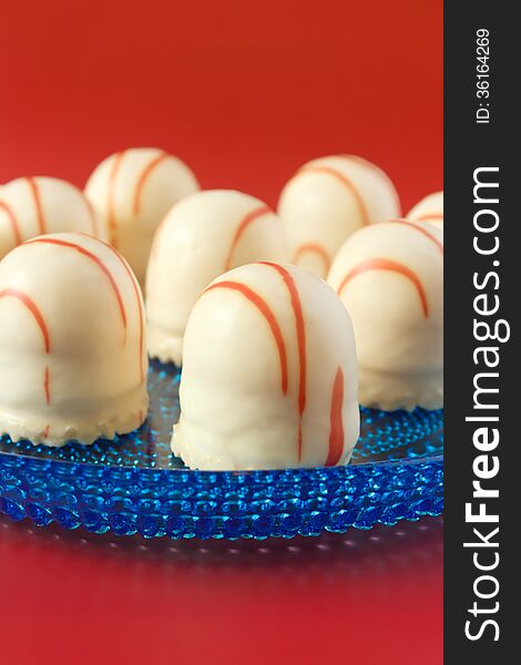 White chocolate coated marshmallow treats on blue glass plate with red background, vertical