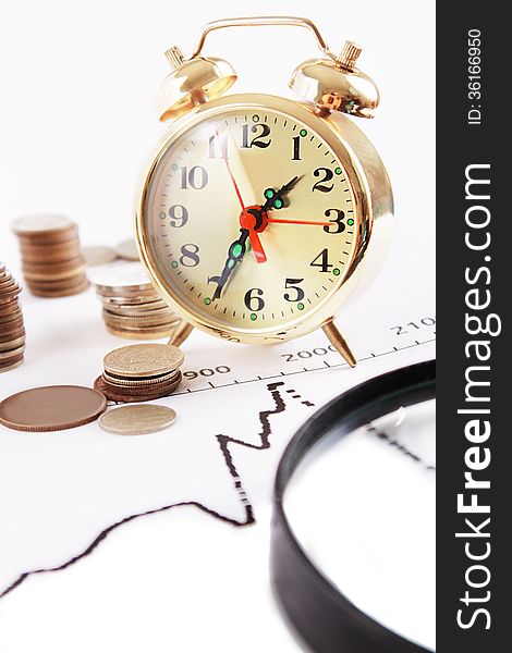 Magnifying glass, alarm clock with pile of coins on growth graphics