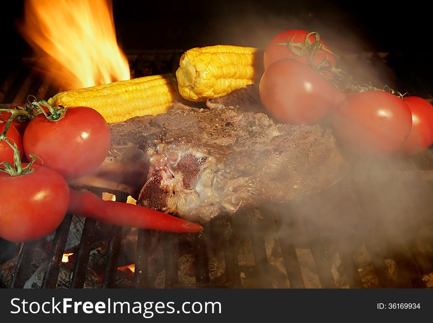 Grilled Rib Steak, tomato and hot Chili Pepper in the Smoke and flames in the BBQ. Grilled Rib Steak, tomato and hot Chili Pepper in the Smoke and flames in the BBQ