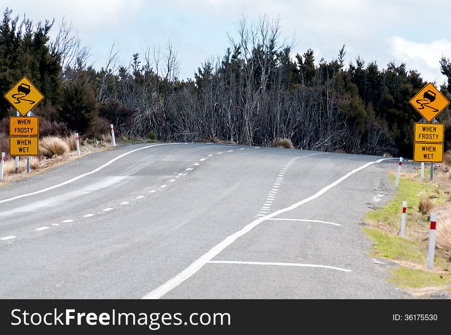 Country road with warning signs leading towards forest