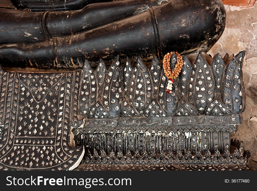 The dried garland hang on the base of black sitting buddha stute in Thailand