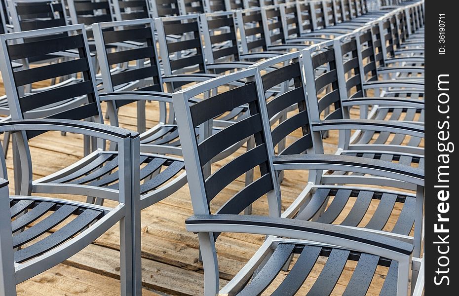 Row of wet chairs on a wooden floor located outdoors in a rainy day. Row of wet chairs on a wooden floor located outdoors in a rainy day.