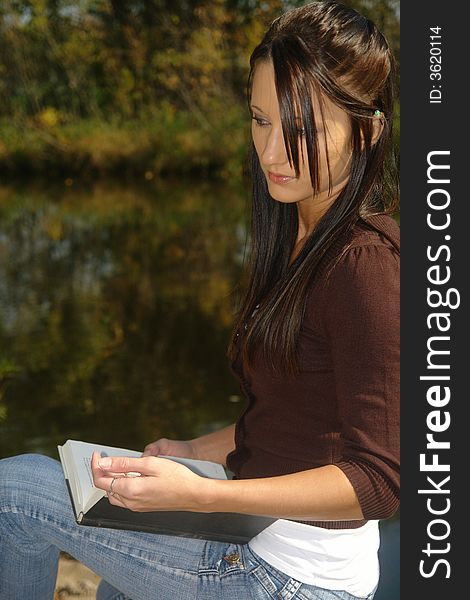 A picture of a beautiful woman reading and comtemplating by water. A picture of a beautiful woman reading and comtemplating by water