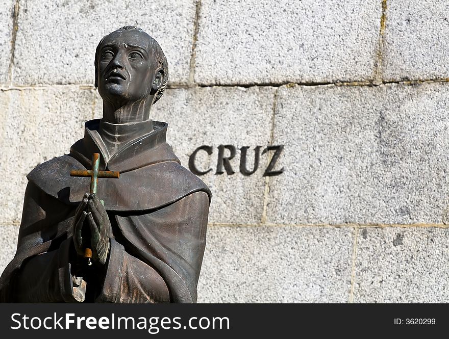 A statue of a friar praying with a cross in his hands and the word cross in Spanish. A statue of a friar praying with a cross in his hands and the word cross in Spanish