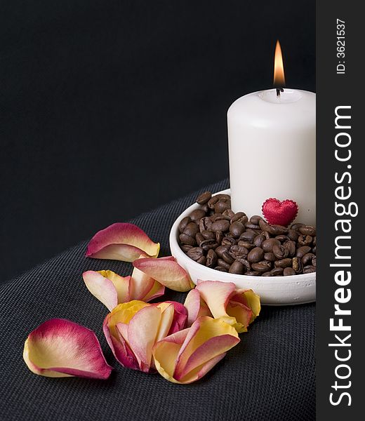 Candle, coffee beans and petals of rose on th black background