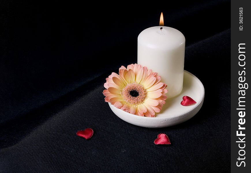 Candle, gerber and red hearts on the black background