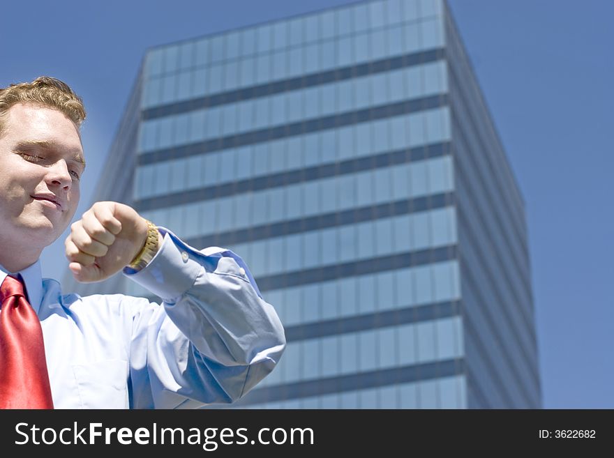 Businessman standing in front of an office building with his arm raised checking his gold watch for the time. Businessman standing in front of an office building with his arm raised checking his gold watch for the time