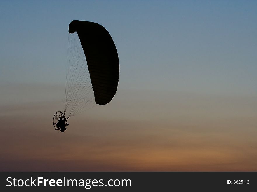 Image of paramotor flying on sunset background