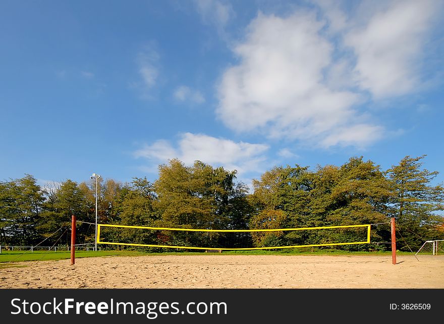 Yellow volleyball net under blue clouded sky, in the background autumn trees