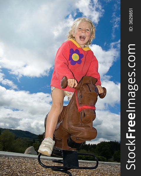 Cute young girl riding a play pony on a sunny day at the park. Cute young girl riding a play pony on a sunny day at the park
