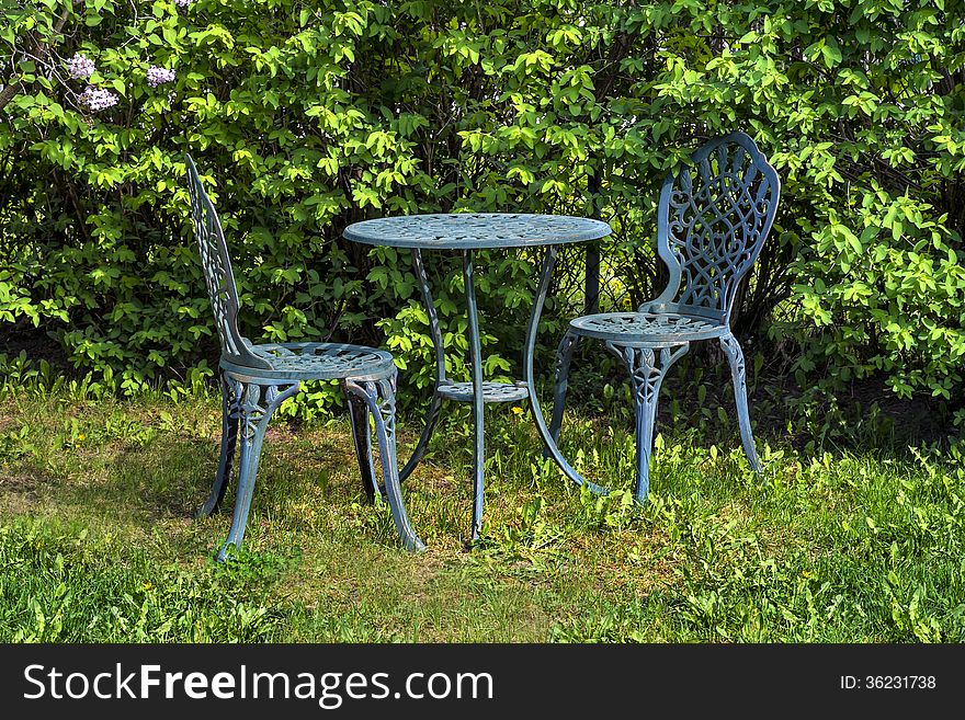 A small green metal table and chairs, are set up and ready for someone to sit and enjoy. A small green metal table and chairs, are set up and ready for someone to sit and enjoy.