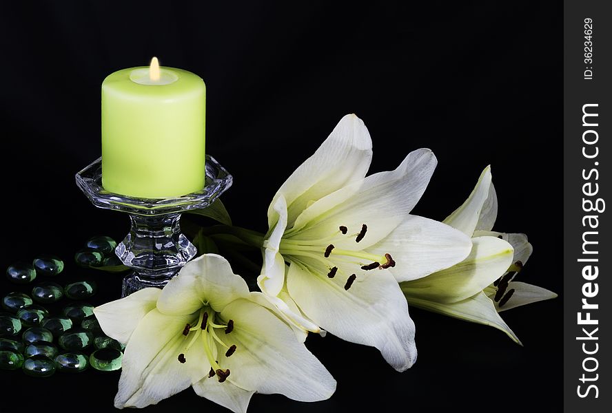 Burning candle and white lilies on a black background