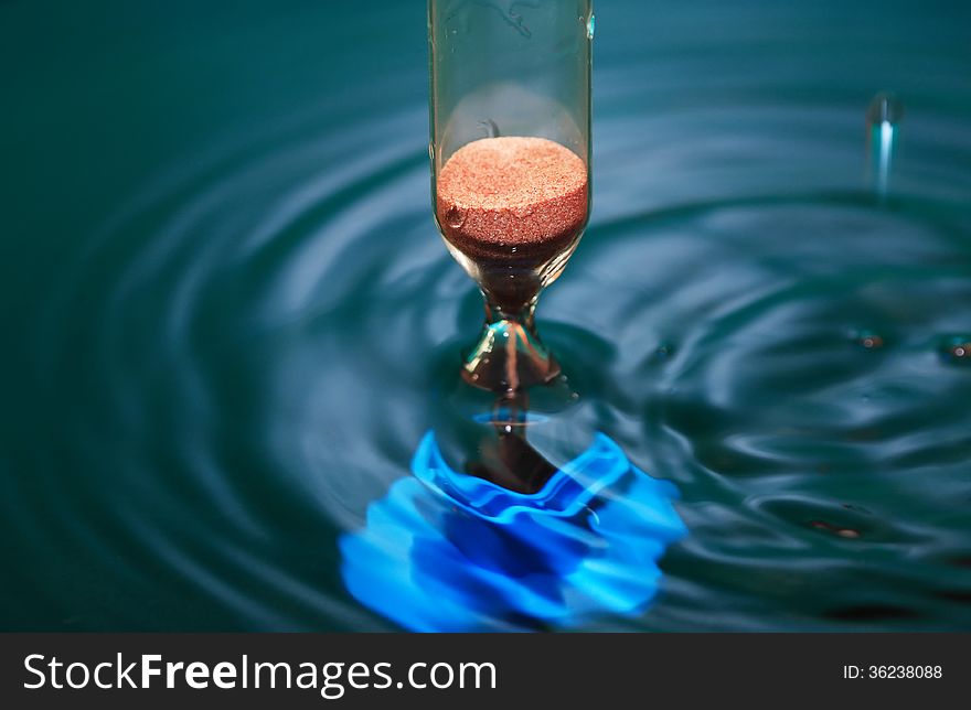 Flow time. Hourglass in dark splashing water. Flow time. Hourglass in dark splashing water