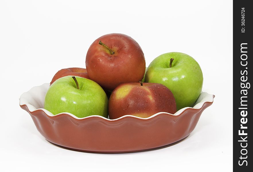 Red and green apples in a red ceramic pie plate against a white background. Red and green apples in a red ceramic pie plate against a white background