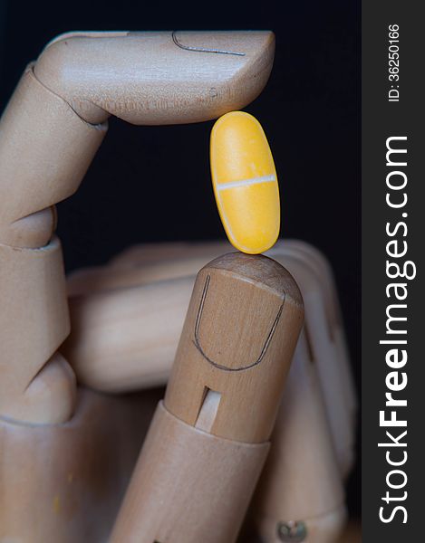 Huge yellow pill between two fingers of a wooden robot like hand.