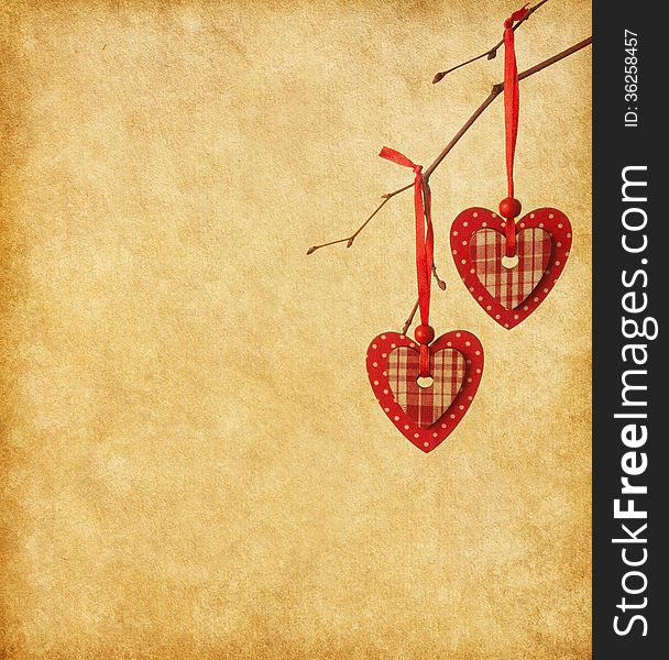 Two red hearts, hanging on a branch over the paper background.