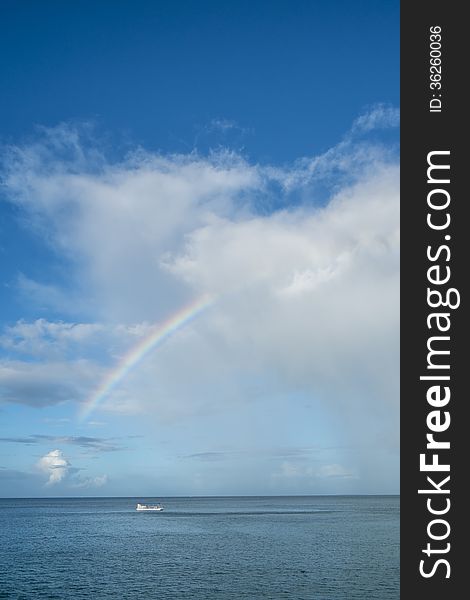 A partial rainbow over the Caribbean ocean with a boat in the foreground.