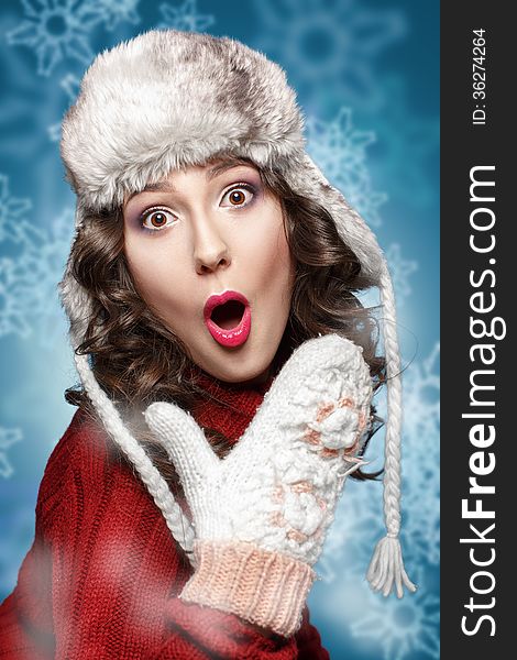 Surprised young woman in winter hat and sweater on a background of snow patterns