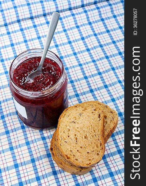 Bread and jar with raspberry jam on blue checked tablecloth