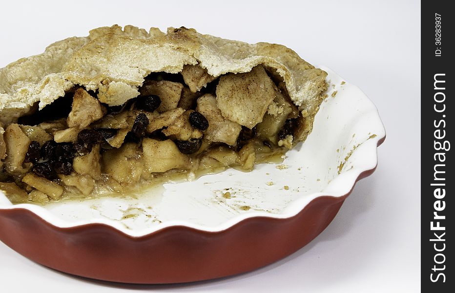 Open half of a homemade apple pie with raisins in a red and white ceramic dish against a white background. Open half of a homemade apple pie with raisins in a red and white ceramic dish against a white background