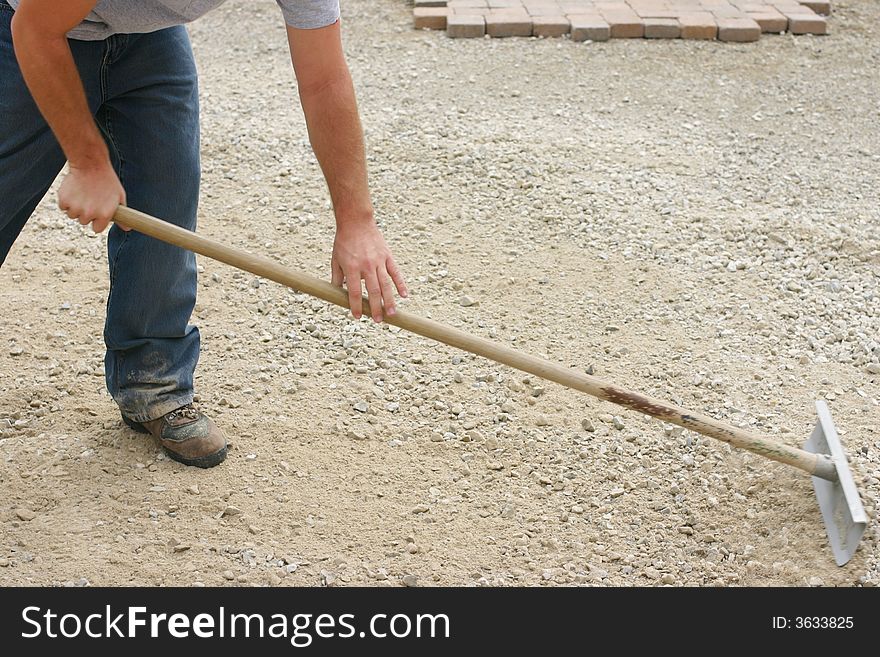 Close up of one male construction worker bending over pushing rake leveling dirt. Close up of one male construction worker bending over pushing rake leveling dirt