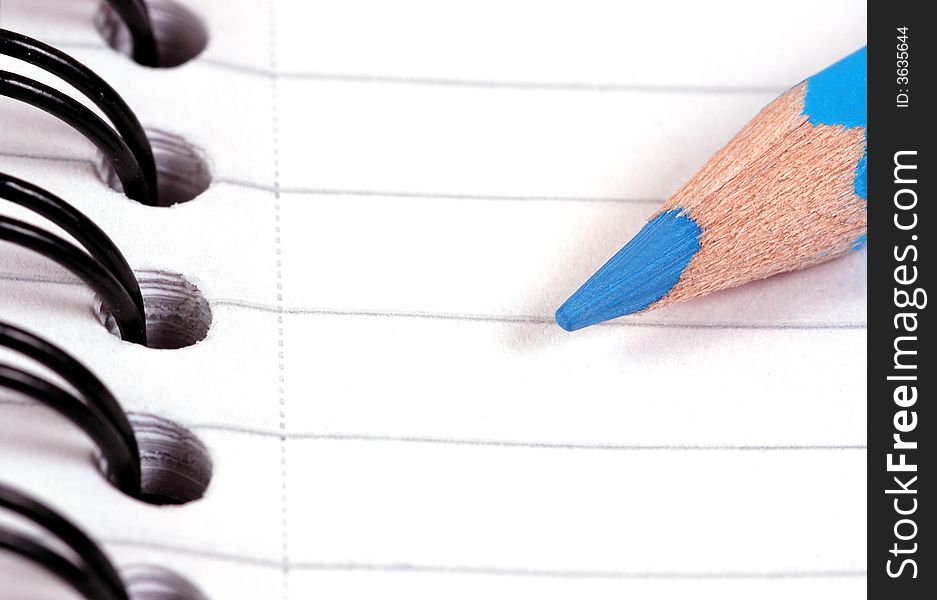 A blue pencil on a ring binded note book.  A macro image taken in a studio. A blue pencil on a ring binded note book.  A macro image taken in a studio.