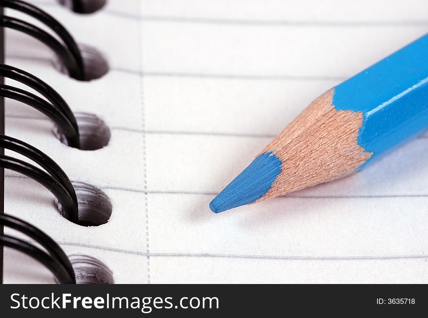 A blue pencil on a ring binded note book. A macro image taken in a studio. A blue pencil on a ring binded note book. A macro image taken in a studio.