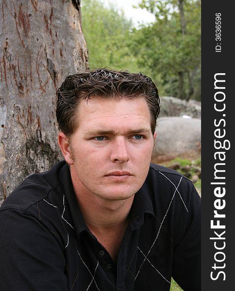 Young Male Model sitting against a tree in the park. Young Male Model sitting against a tree in the park