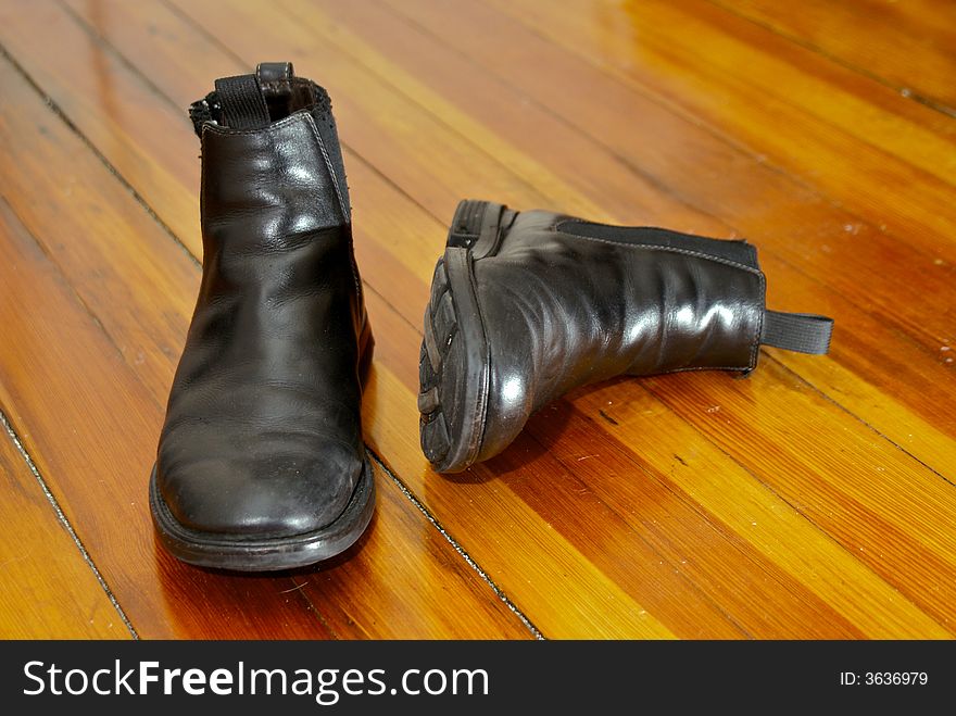 Pair of old black leather boots in the sunshine on a dirty pine wood floor