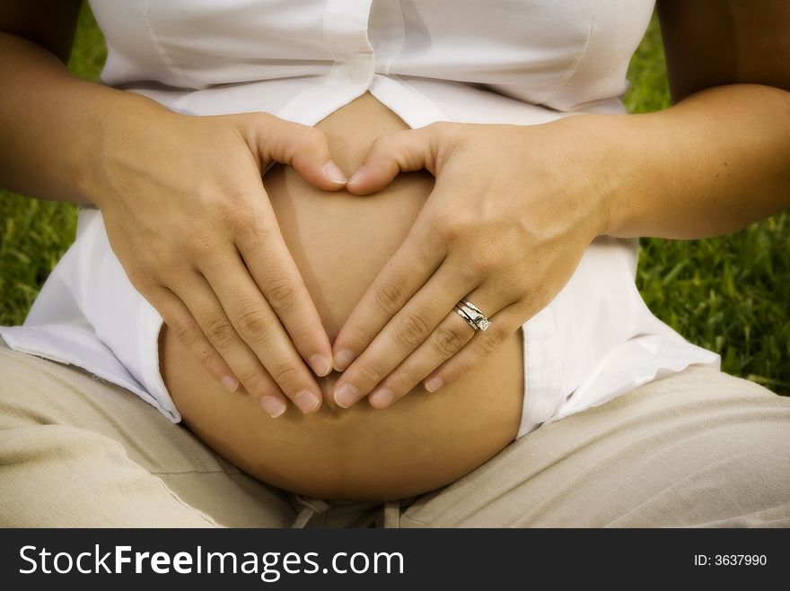 Mother to be makes a heart shape on her tummy with her hands. Mother to be makes a heart shape on her tummy with her hands