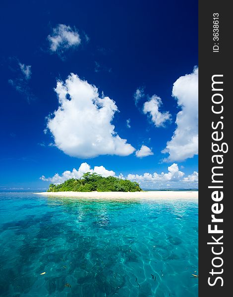 Beautiful tropical island vacation paradise with white sand, tall palm trees, fluffy white clouds, a dark blue sky and surrounded by turquoise water and coral reef