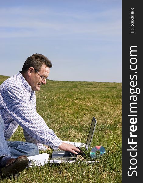 Businessman sittingloo on the grass with his laptop, seen from the profile. Businessman sittingloo on the grass with his laptop, seen from the profile.