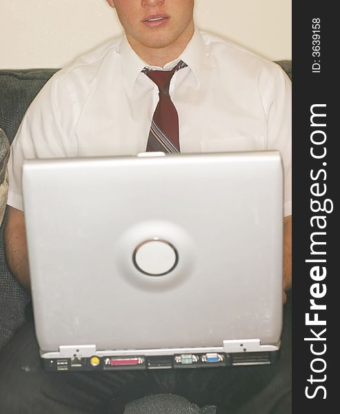 Front close-up view of young man with loose tie holding laptop on knees as he sits on sofa. Front close-up view of young man with loose tie holding laptop on knees as he sits on sofa