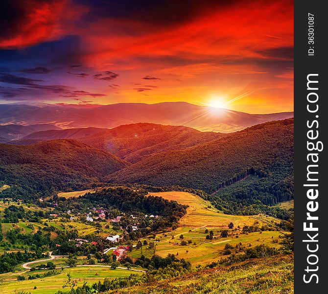 Autumn landscape. village on the hillside. forest on the mountain covered with red and yellow leaves. over the mountains the beam of light falls on a clearing at the top of the hill. Autumn landscape. village on the hillside. forest on the mountain covered with red and yellow leaves. over the mountains the beam of light falls on a clearing at the top of the hill.