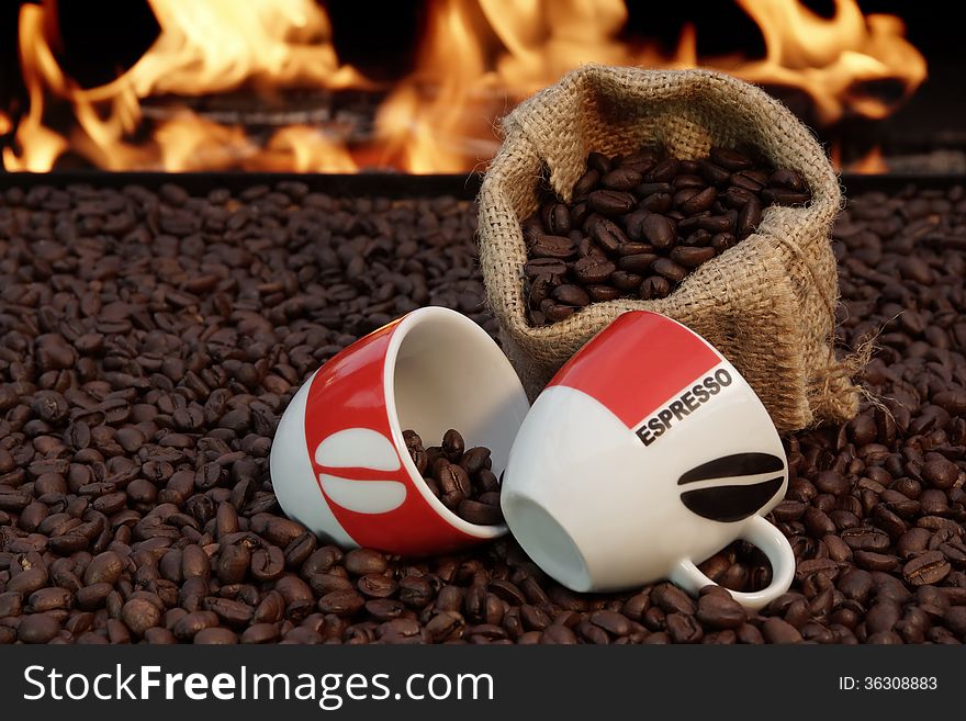 Two ceramic cups and a jute sack with coffee beans on a background of fire. Two ceramic cups and a jute sack with coffee beans on a background of fire