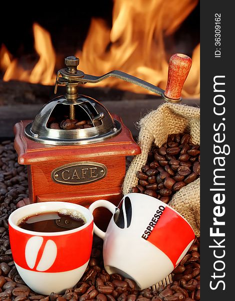 Two ceramic cups, jute sack with coffee beans and coffee grinder on a background of fire. Two ceramic cups, jute sack with coffee beans and coffee grinder on a background of fire