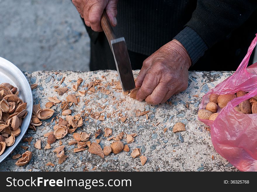 Senior woman is breaking almonds with a metal hammer. Senior woman is breaking almonds with a metal hammer.