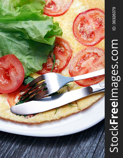 Closeup of fork and knife on plate with omelet and tomatoes. Closeup of fork and knife on plate with omelet and tomatoes