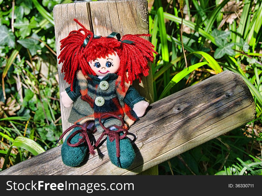 Raggedy doll sitting on some wooden railing in open-shade.