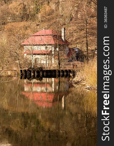 House with red roof is reflected on the surface of the river. House with red roof is reflected on the surface of the river