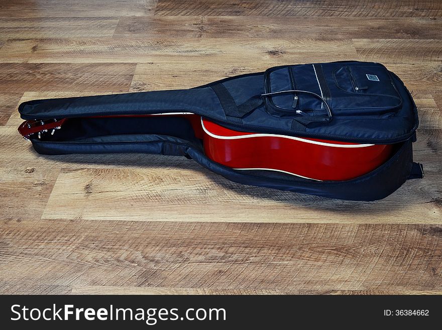 Red classical guitar in a black soft case on a wooden floor. Red classical guitar in a black soft case on a wooden floor