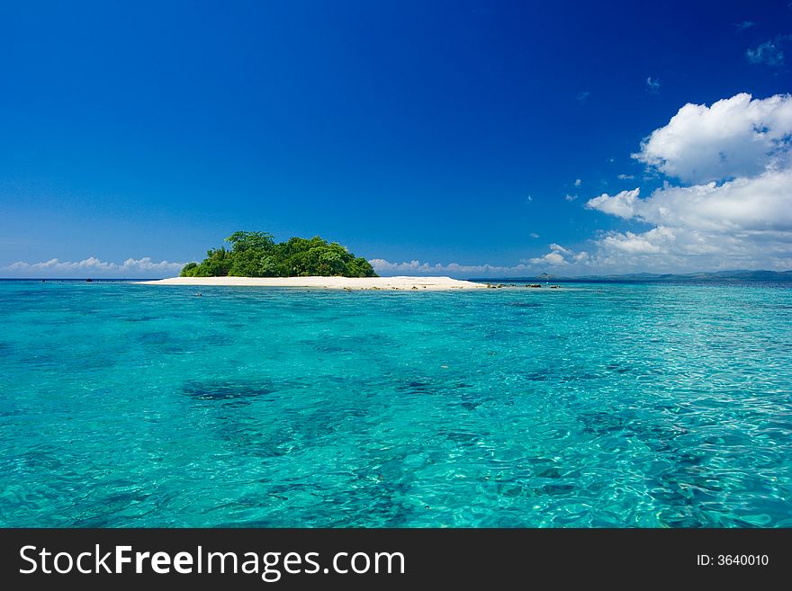 Beautiful tropical island vacation paradise with white sand, tall palm trees, fluffy white clouds, a dark blue sky and surrounded by turquoise water and coral reef