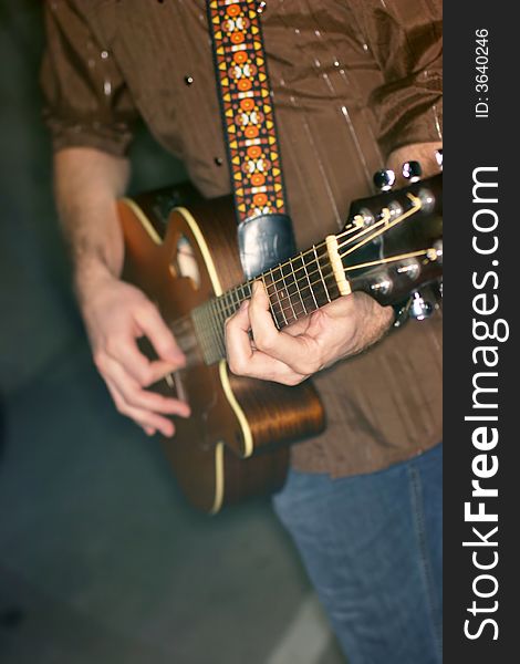 Close-up view of midsection of man holding guitar wearing jeans and brown shirt. Close-up view of midsection of man holding guitar wearing jeans and brown shirt