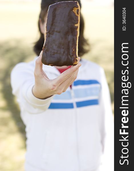 Close-up shot of young woman wearing casual clothing holding, displaying chocolate donut bar, waist-up. Close-up shot of young woman wearing casual clothing holding, displaying chocolate donut bar, waist-up